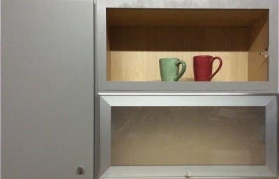 wall cabinets with one slab door in painted gray, one aluminum-frame glass door and one open cabinet with red and green mugs displayed