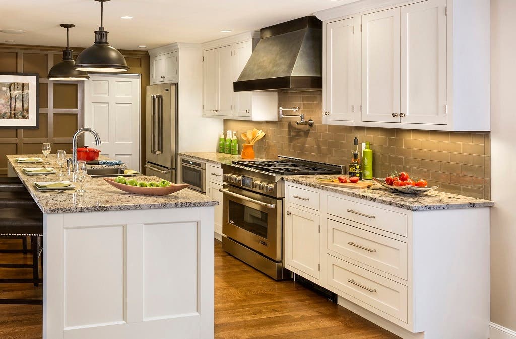 kitchen with white inset shaker cabinets, long stainless bar pulls, metal range hood and oil brushed steel island pendants