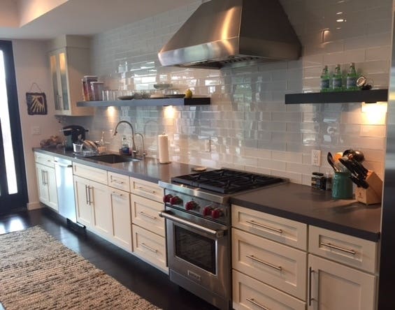 long kitchen wall with white shaker base cabinets, white subway tile wall, open shelves and one glass-door cabinet