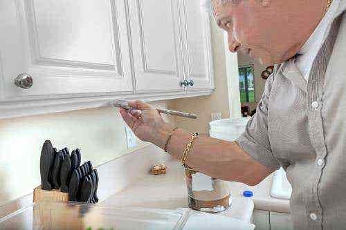 Man hand-painting white raised panel wall cabinets with chrome knobs Man hand-painting white raised panel wall cabinets with chrome knobs