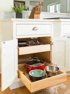 Double roll-out trays storing bowls, pots, and a colander. Featuring an White inset styled base cabinet Double roll-out trays storing bowls, pots, and a colander. Featuring an White inset styled base cabinet