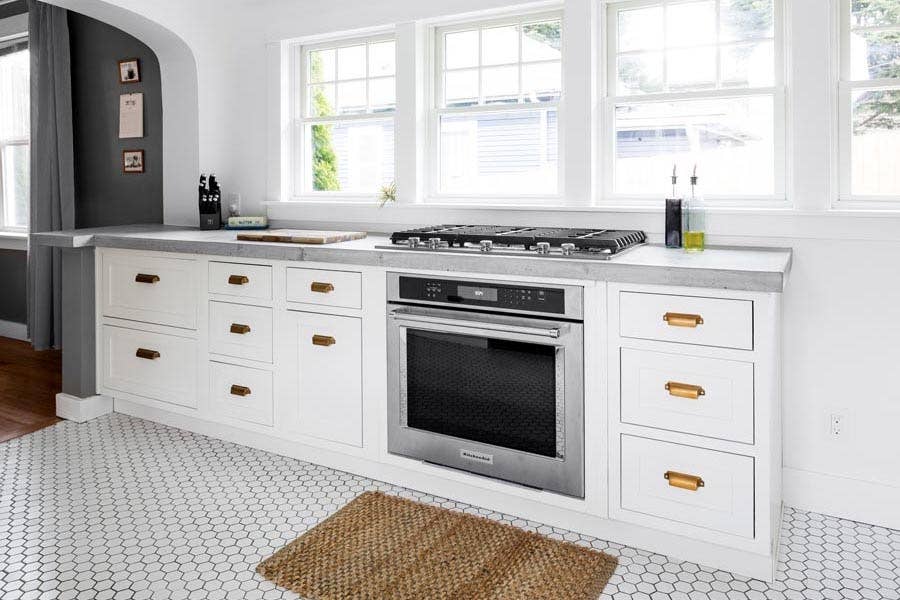 White inset cabinets with built-in oven and cooktop under a large kitchen window