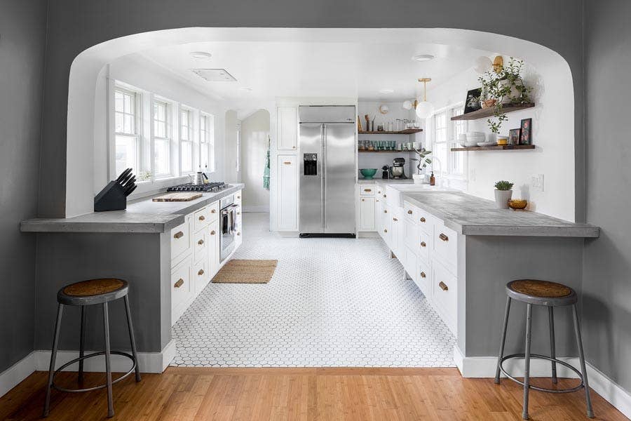 Bright white and gray galley kitchen with concrete countertops, white cabinets and stainless steel appliances