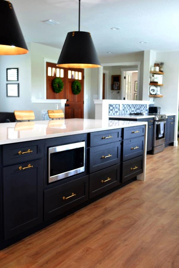CliqStudios Shaker cabinets in Black used in a kitchen island with a white waterfall countertop. A base microwave sits in the center of the island, and pendant lighting with black shades hang above. CliqStudios Shaker cabinets in Black used in a kitchen island with a white waterfall countertop. A base microwave sits in the center of the island, and pendant lighting with black shades hang above.