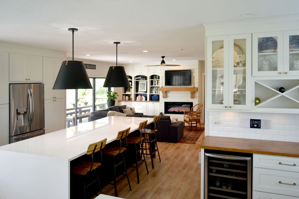 Large white shaker kitchen with white waterfall countertop island, black pendants, and a wine bar