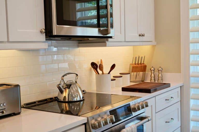Stainless steel stove and microwave surrounded by white shaker cabinets, subway tile backsplash and white countertops
