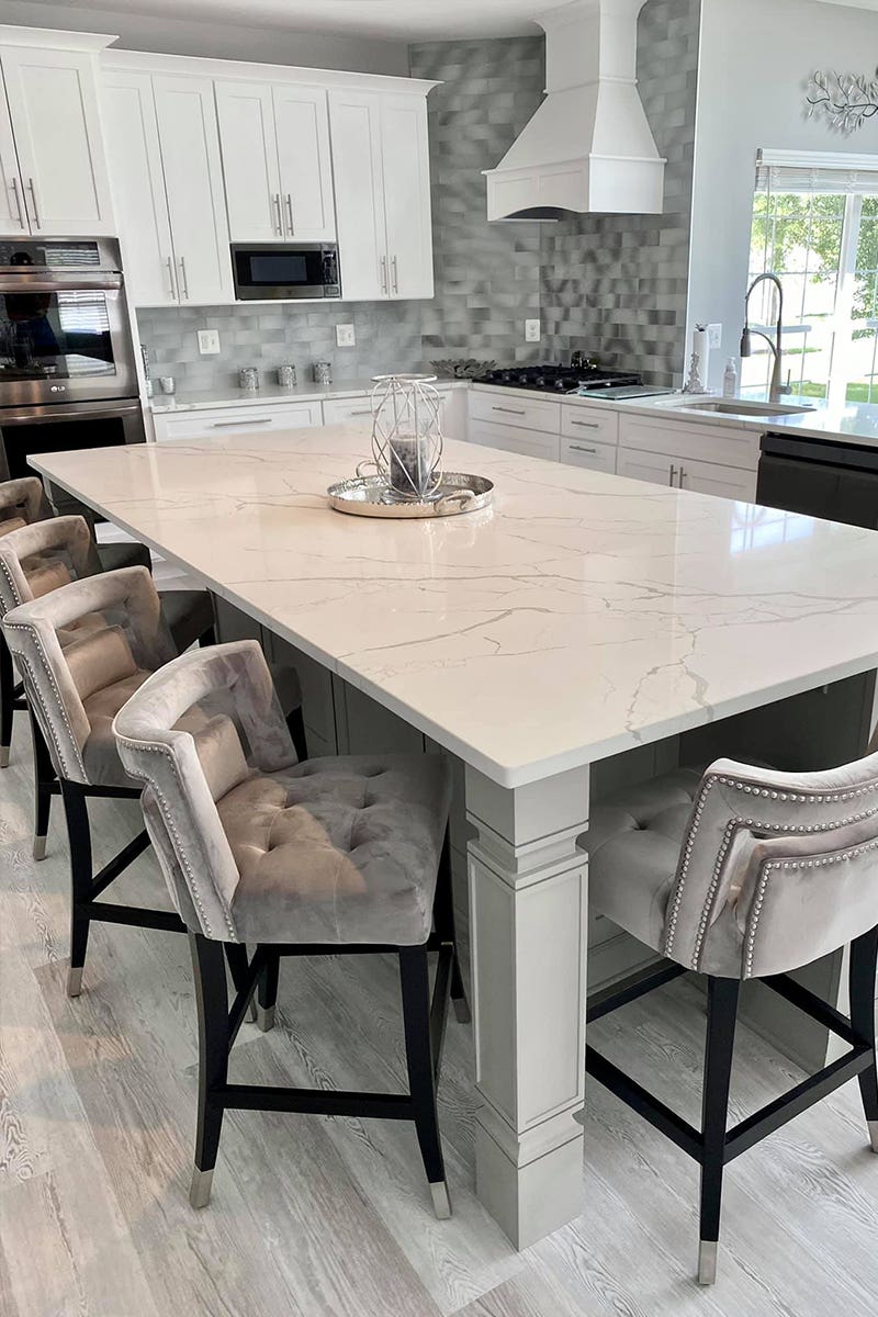 L-shaped open shaker white kitchen with decorative hood and large island with furniture legs L-shaped open shaker white kitchen with decorative hood and large island with furniture legs