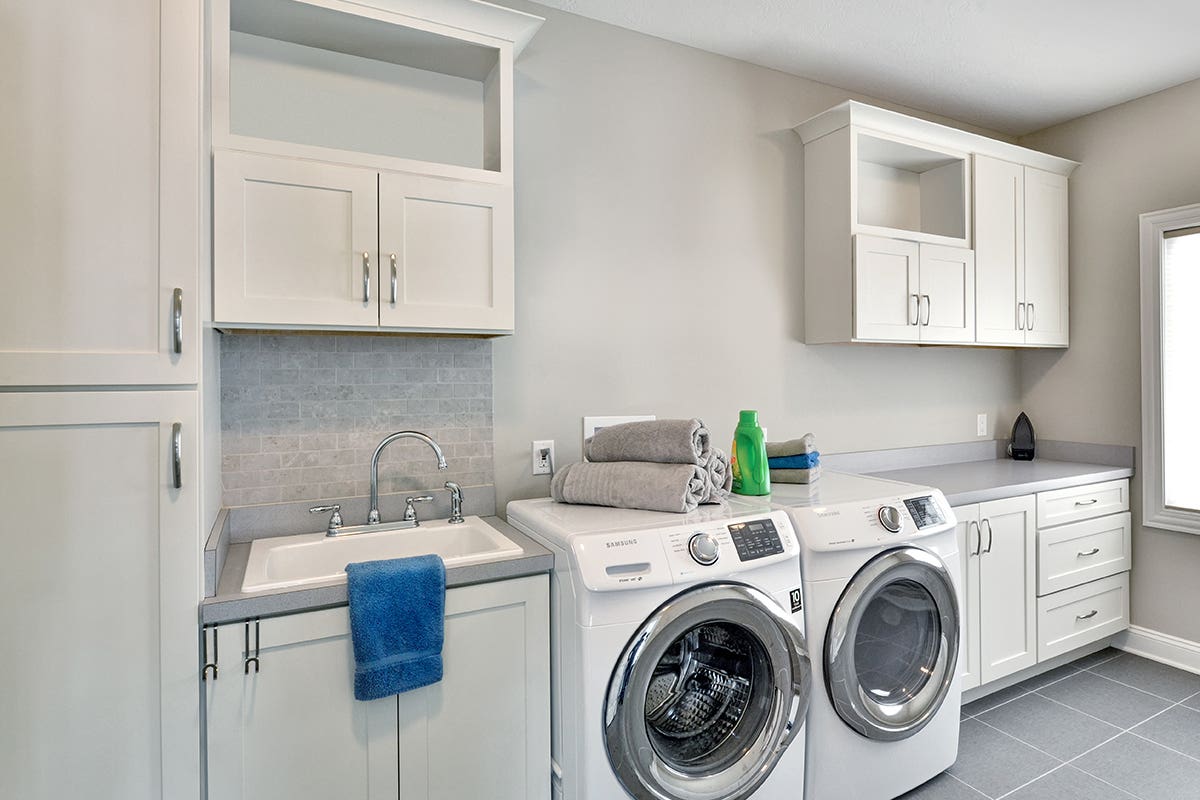 White shaker laundry room cabinets with washer/ dryer centered and gray laminate countertop space