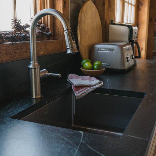 Dark blue/gray soapstone countertop with white veining, a brushed nickel gooseneck faucet, and stainless steel sink