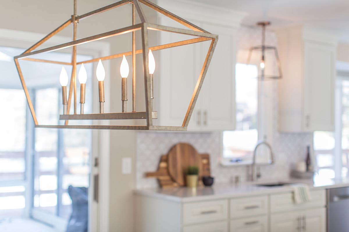 White raised panel kitchen design with white tile backsplash and a Traditional gold chandelier above the dining room table.