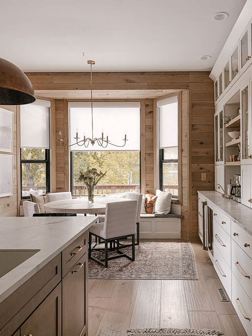 Light wood paneled breakfast nook with large window tucked in next to medium brown stained island and white shaker buffet kitchen cabinets Light wood paneled breakfast nook with large window tucked in next to medium brown stained island and white shaker buffet kitchen cabinets