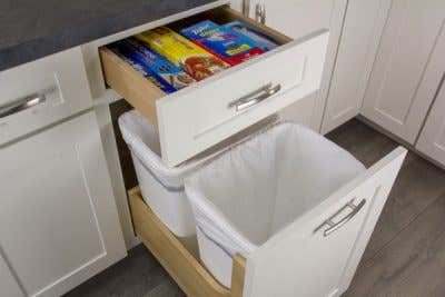 Empty wastebaskets in an open wastebasket cabinet. Above it, a drawer is open containing boxes.