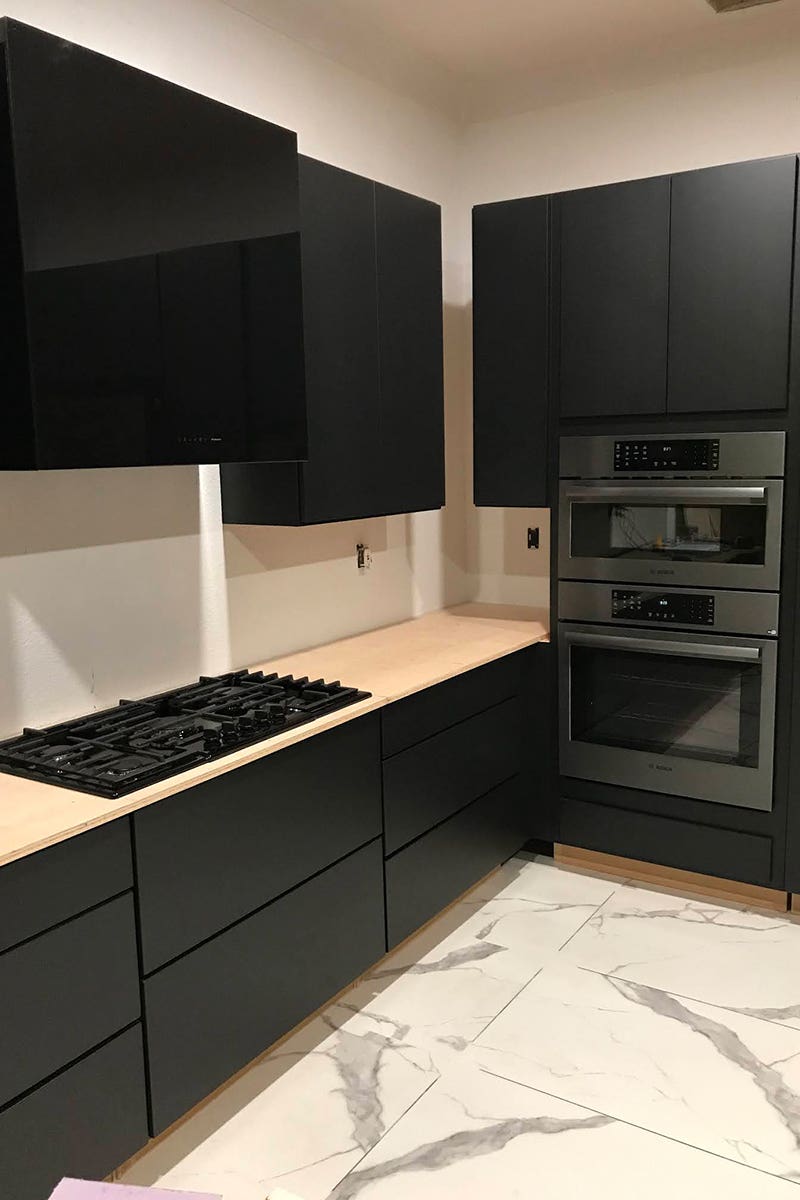Black painted kitchen cabinets in slab door, dark appliances, and white marble tiled floors Black painted kitchen cabinets in slab door, dark appliances, and white marble tiled floors