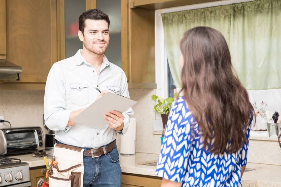 Contractor standing in front of outdated kitchen cabinets presenting remodeling options to a homeowner Contractor standing in front of outdated kitchen cabinets presenting remodeling options to a homeowner