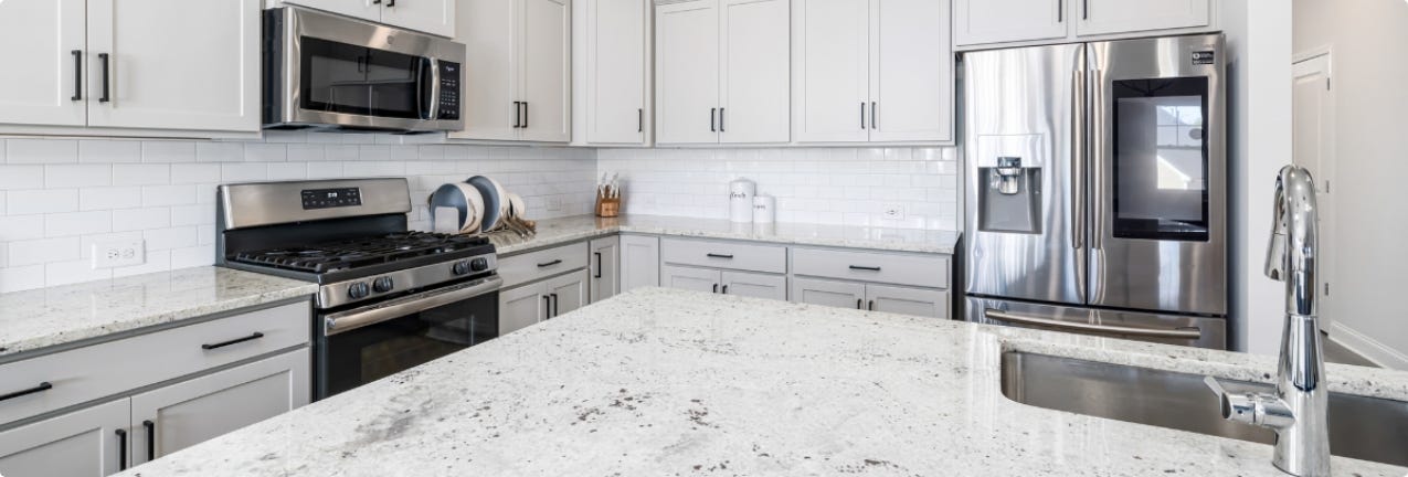 What You Need to Know About Granite & Quartz L-shaped white shaker kitchen design with white granite countertops and island