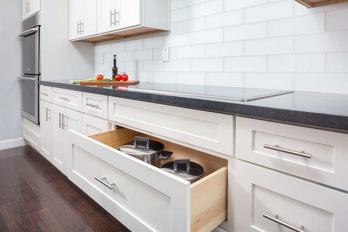 modern kitchen cooktop wall has deep drawer storage, black granite countertops, white shaker cabinets, built in wall ovens and large white glass subway tile backsplash