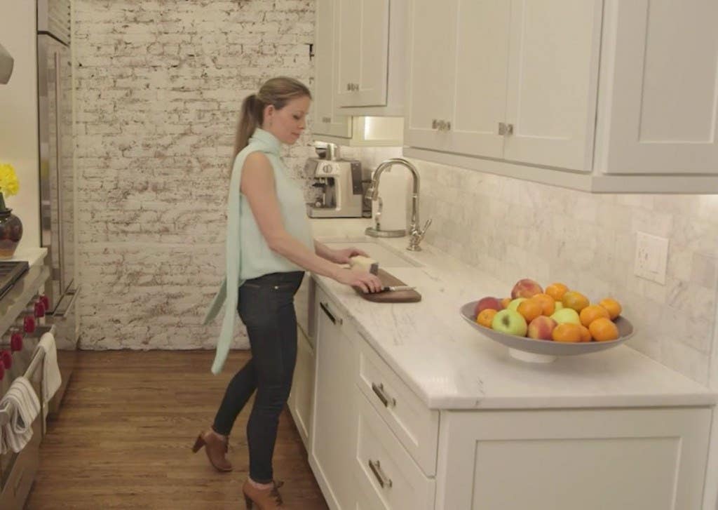 woman in kitchen with white cabinets, white marble countertops and paneled dishwasher cuts fruit