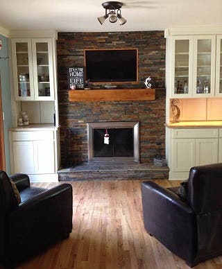 Fireplace with ceiling height stone facing framed by white shaker display cabinets with glass doors