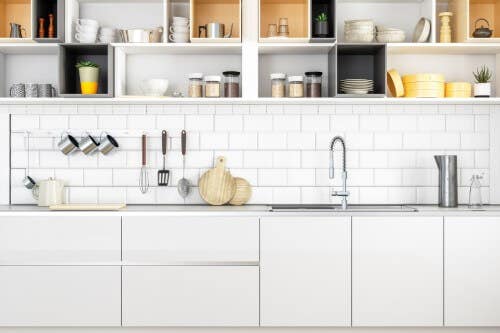 Modern white slab kitchen cabinets with open kitchen cabinet storage above filled with food storage, cups and bowls Modern white slab kitchen cabinets with open kitchen cabinet storage above filled with food storage, cups and bowls