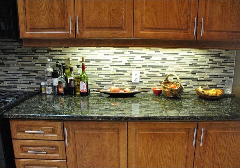 Raised panel cherry wood base cabinets with brushed nickel pulls and a green patterned granite countertop.