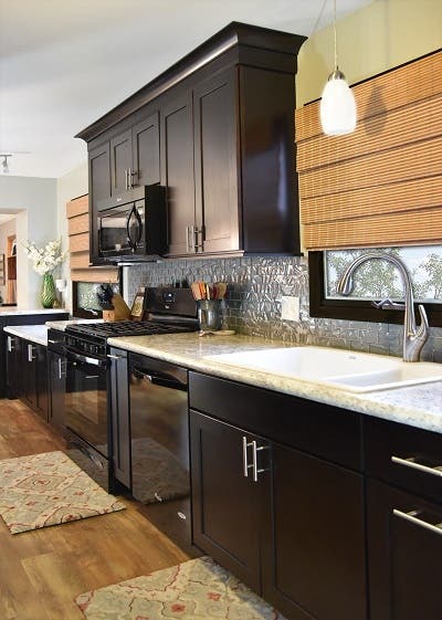 long kitchen wall has black birch cabinets with stacked crown molding, brushed stainless bar pulls, glass subway tile and oversized double sink