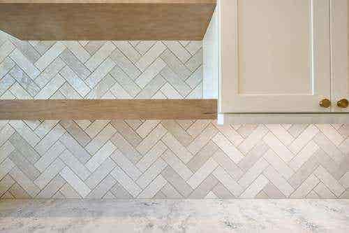 White shaker cabinets with a light cream herringbone tile backsplash and light wood floating shelves White shaker cabinets with a light cream herringbone tile backsplash and light wood floating shelves