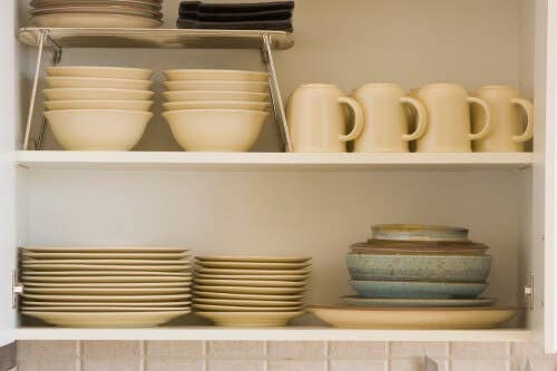 White open kitchen cabinet with organized plates, bowls and cups inside White open kitchen cabinet with organized plates, bowls and cups inside