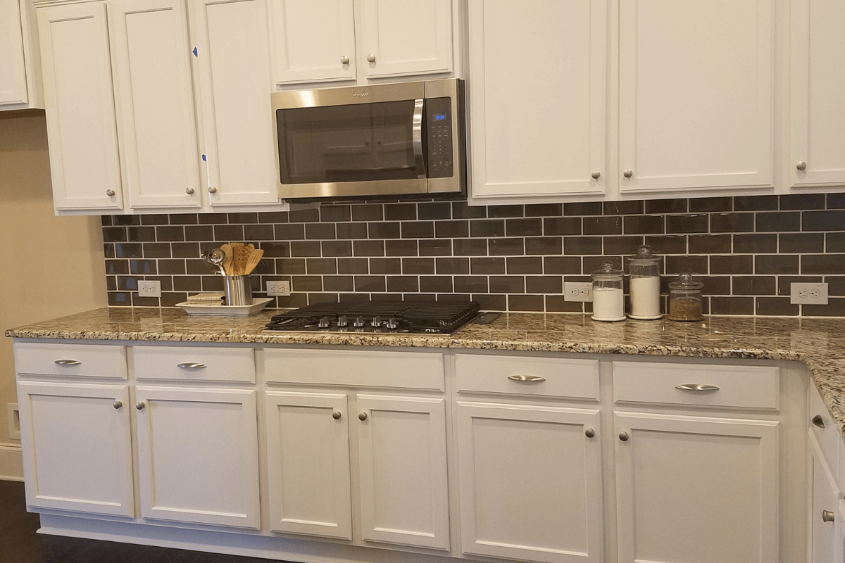 White shaker kitchen cabinets Cooktop wall of a white shaker kitchen design with partial overlay kitchen cabinets, granite countertops and a stainless steel microwave.