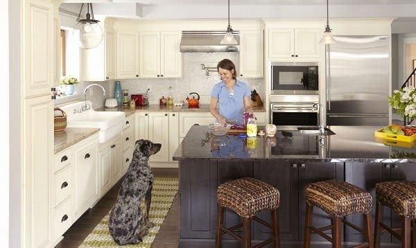 woman cooking at center island smiles at large dog sitting nearby in kitchen with cream raised panel cabinets on perimeter and dark furniture look island woman cooking at center island smiles at large dog sitting nearby in kitchen with cream raised panel cabinets on perimeter and dark furniture look island